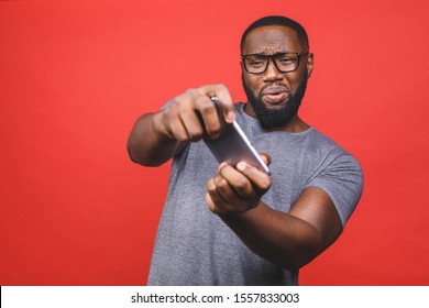 Portrait Of A Cheerful Young Black African American Man Dressed In Casual Playing Games On Mobile Phone Isolated Over Red Background.