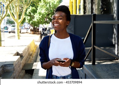 Portrait of cheerful young black woman walking outdoors with mobile phone - Shutterstock ID 453709894