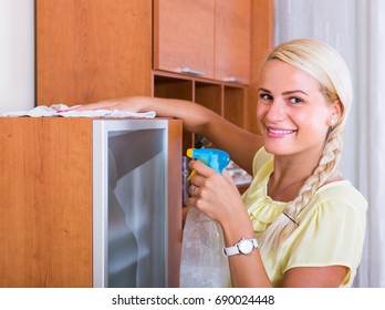 Portrait Of Cheerful Young Blonde Woman Dusting Furniture At Home
