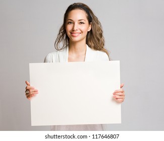 Portrait of a cheerful young brunette woman holding a white blank banner.
