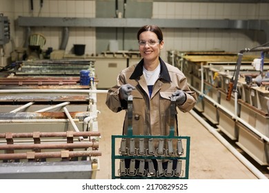 Portrait Of Cheerful Young Brunette Woman In Protective Eyewear Standing At Factory And Carrying Metal Belt Parts In Frame