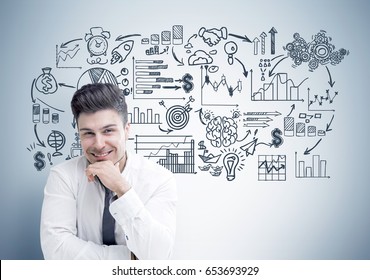 Portrait cheerful young businessman sitting near gray wall and his business scheme sketch drawn behind his back 
