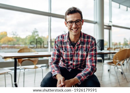 Portrait of a cheerful young businessman sitting in office. Happy young professional smiling at camera.