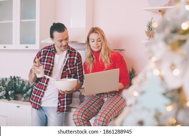 Portrait Of A Cheerful Young Couple Cooking Christmas Meal Together According To A Recipe On A Tablet Computer