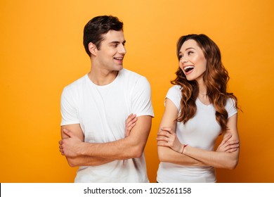 Portrait of a cheerful young couple standing with arms folded and looking at each other isolated over yellow background