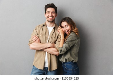 Portrait of a cheerful young couple standing together isolated over gray background, hugging