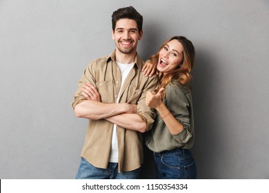 Portrait of a cheerful young couple standing together isolated over gray background, showing thumbs up - Powered by Shutterstock