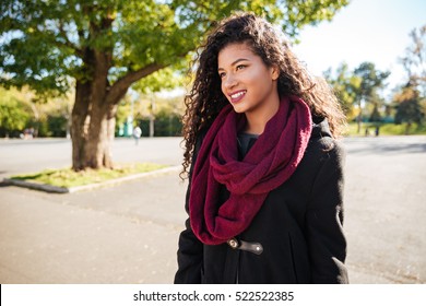Portrait of cheerful young dark skinned curly woman wearing scarf against nature background. Look aside.