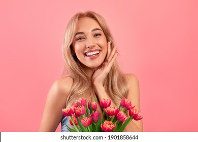 Portrait of cheerful young lady with romantic spring bouquet of tulips over pink studio background. Gorgeous blonde enjoying Woman's Day celebration, receiving flowers as special gift - Shutterstock ID 1901858644