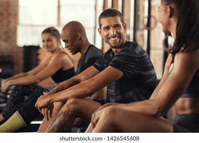 Portrait of cheerful young man sitting at rowing machine and talking with woman at gym. Smiling sportsman relaxing after workout with his friends at gym. Smiling guy and girl having conversation. - Powered by Shutterstock