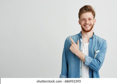 Portrait Of Cheerful Young Man Smiling Looking At Camera Pointing Finger Up Over White Background.