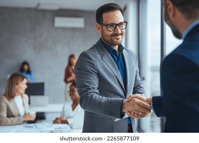 Portrait of cheerful young manager handshake with new employee. Business partnership meeting in office. Close up of handshake in the office. Mature businessman shake hands with a younger colleague - Powered by Shutterstock