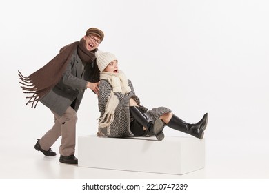 Portrait Of Cheerful Young People, Man And Woman In Winter Clothes Having Fun Together, Sledding Over White Background. Concept Of Retro Fashion, Style, Friendship, Creativity, Youth, Emotions, Ad