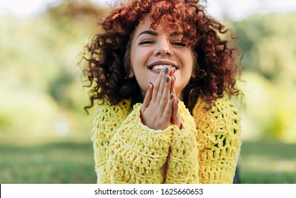 Portrait of cheerful young woman with curly hair smiling broadly with toothy smile. Female has positive expression, wearing yellow sweater and posing against nature background. People, lifestyle - Powered by Shutterstock