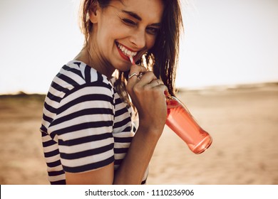 Portrait of cheerful young woman drinking beverage with straw from glass bottle. Girl drinking a soda outdoors on a summer day.