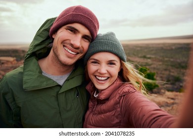 Portrait of cheerful young woman embracing man in winter clothing taking selfie during camping on mountain - Powered by Shutterstock