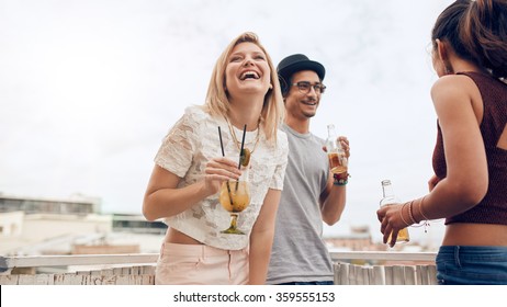 Portrait Of Cheerful Young Woman Enjoying Party With Her Friends. Young People Having Fun At Rooftop Party. They Are Laughing And Having Cocktail Drinks.