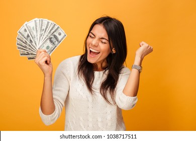Portrait of a cheerful young woman holding money banknotes and celebrating isolated over yellow background - Shutterstock ID 1038717511