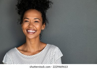 Portrait of cheerful young woman laughing against grey background. Happy african american girl with curly hair smiling against gray wall with copy space. Close up face of young black woman smiling. - Powered by Shutterstock