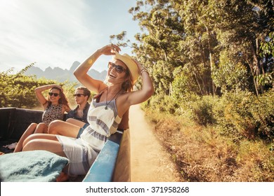 Portrait of a cheerful young woman sitting in the back of pickup truck with friends. Young people enjoying on a road trip. - Powered by Shutterstock