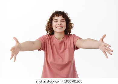 Portrait Of Cheerful Young Woman Spread Hands Sideways, Reaching For Hugs And Warm Welcome, Smiling Happy And Friendly At Camera, Standing Against White Background