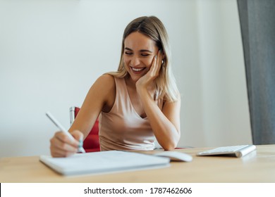 Portrait of a cheerful young woman writing in note pad, close-up.