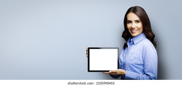 Portrait Of Cheerfully Smiling Brunette Businesswoman Showing Mock Up Blank Tablet Pc, Ipad Touchpad With Copy Space Area For Text, Over Grey Color Background. Confident Young Business Woman At Studio