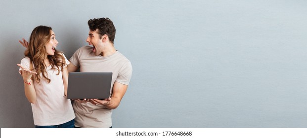 Portrait of a cheery happy couple holding laptop computer while standing and celebrating isolated over gray wall background - Shutterstock ID 1776648668