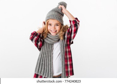 Portrait Of A Cheery Little Girl Dressed In Winter Hat And Scarf Posing And Looking At Camera Isolated Over White Background