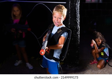 Portrait Of Cheery Tweenager Boy With Laser Gun Having Fun On Dark Lasertag Arena