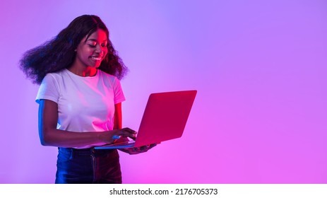 Portrait of cheery young black woman using laptop pc, studying or working remotely, having online conference in neon light, banner with empty space. African American lady with computer browsing web - Shutterstock ID 2176705373