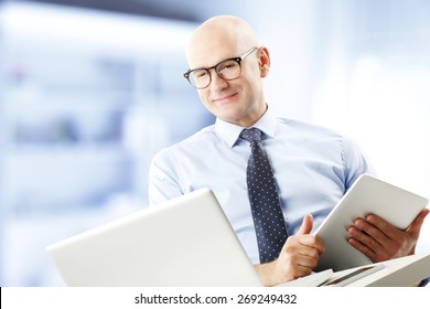 Portrait Of Chief Financial Officer Holding Financial Report In Hands While Sitting In Front Of Laptop And Analyzing Data. Businessman Working At Office. 