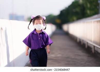 Portrait Of Child 3-4 Years Old. Little Girl Wearing White Cloth Face Mask To Prevent Spread Virus And Toxic Dust PM2.5, Air Pollution. Kindergarten Kid Walking To School In Morning. Sweet Smile.