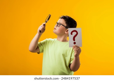 Portrait of child boy with glasses on face looking through magnifier and holding question mark card over yellow background. Education and curiosity concept - Powered by Shutterstock