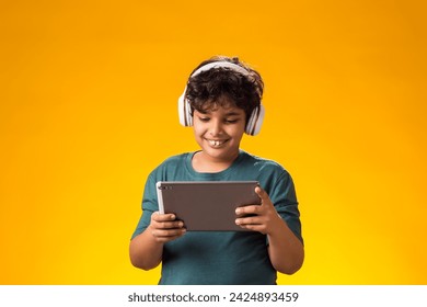 Portrait of child boy using digital tablet and headphones and playing video game over yellow background. Leisure and gadget addiction concept. - Powered by Shutterstock