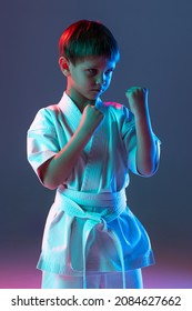 Portrait Of Child, Concentrated Sportsman Training, Practising Karate Isolated Over Gradient Blue Background In Neon. Concept Of Martial Art, Healthy Lifestyle, Sport, Action, Combat Sport And Ad