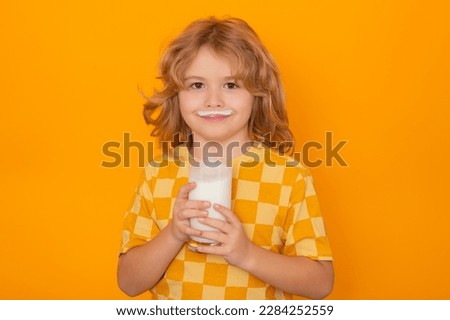 Portrait of child drinking milk, yellow isolated studio background. Kid with glass of milk and milk moustache.