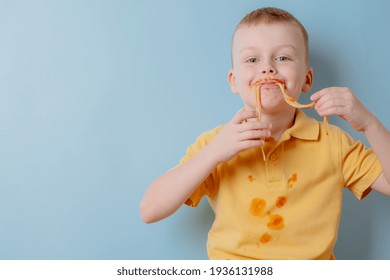 Portrait of a child eating spaghetti with hands. Boy stained with tomato sauce. isolated on blue background. High quality photo