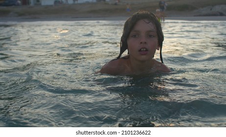 Portrait Of A Child Floating In The Sea Near The Shore In The Evening At Sunset. Outdoor Water Safety.