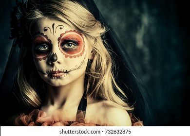 Portrait Of A Child Girl In A Costume Of Calavera Catrina Over Dark Grunge Background. Little Girl With Sugar Skull Makeup. Halloween Party. Dia De Los Muertos. Day Of The Dead. 