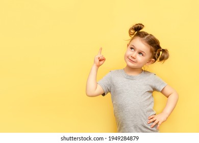 Portrait Of Child Girl With Finger Pointed Up. Little Kid In Pose Has Idea Isolated On Yellow Blackboard. Success, Bright Idea, Creative Ideas And Innovation Technology Concept