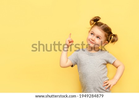 Portrait of child girl with finger pointed up. Little kid in pose has idea isolated on yellow blackboard. Success, bright idea, creative ideas and innovation technology concept