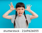 portrait of a child girl happy positive smile shows a grimace stuck out tongue isolated on a blue background spread fingers.