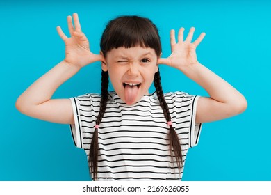 portrait of a child girl happy positive smile shows a grimace stuck out tongue isolated on a blue background spread fingers.