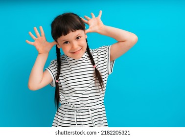 portrait of a child girl happy positive smile fooling around isolated on a blue background spread fingers in ears