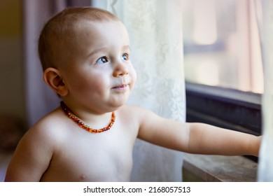 Portrait of child looking at window in the morning. A toddler boy wearing amber necklace, painless teething concept, natural pain reliever