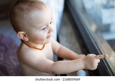 Portrait of child looking at window in the morning. A toddler boy wearing amber necklace, painless teething concept, natural pain reliever