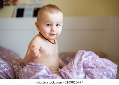 Portrait of a child sitting in a bed under quilt. A boy wearing amber necklace, painless teething