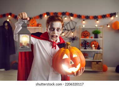 Portrait Of Child In Spooky Vampire Costume. Kid Dressed As Count Dracula Holding Lamp And Jack-o-lantern. Teen Boy In Cape With Crazy Eyes And Fake Blood Makeup Looking For Candy On Halloween Night