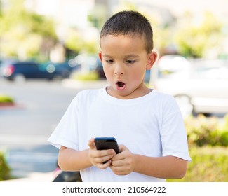 Portrait Child, Surprised Boy, Little Man Texting On Mobile Using Smart Phone Isolated Outdoor, Outside Background. Funny Looking Human Face Expression, Emotion, Reaction, Body Language. Communication